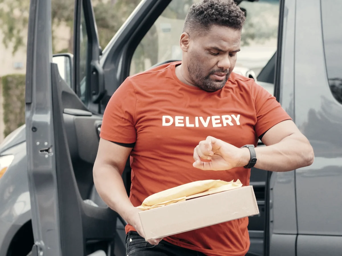 Delivery driver checking his watch while carrying a parcel from the van