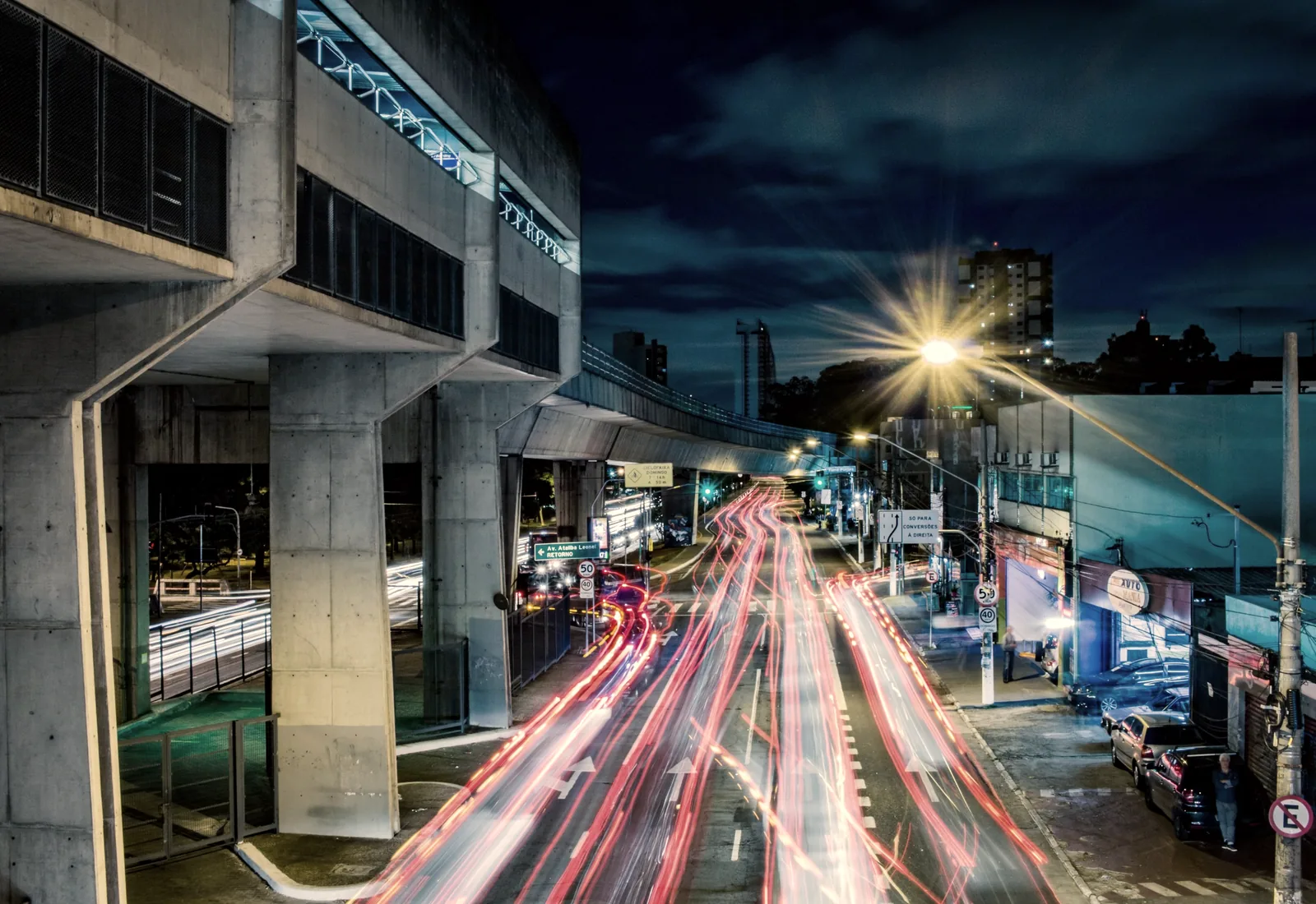 Long exposure tail lights streaking beneath minimalist concrete architecture at night