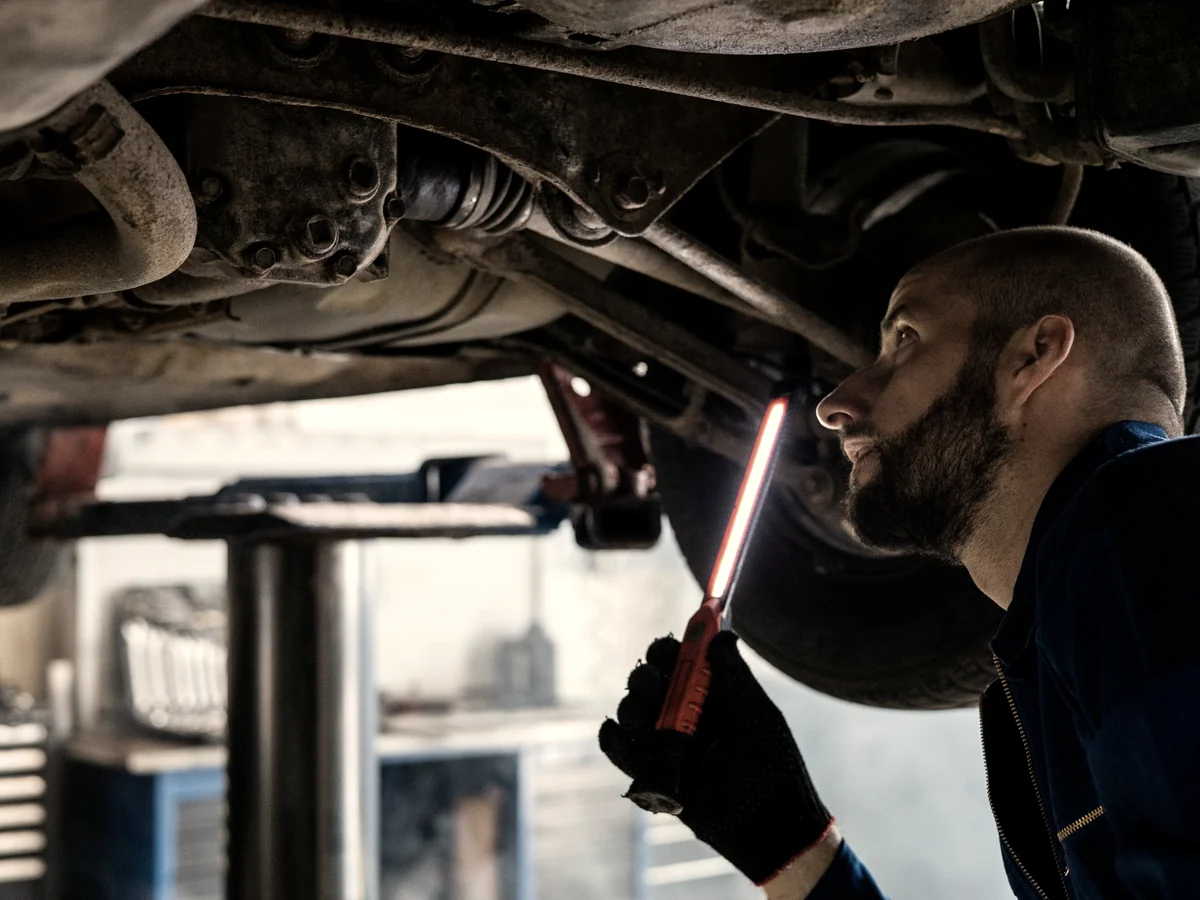 Technician inspecting the underbody of a raised vehicle with a work light