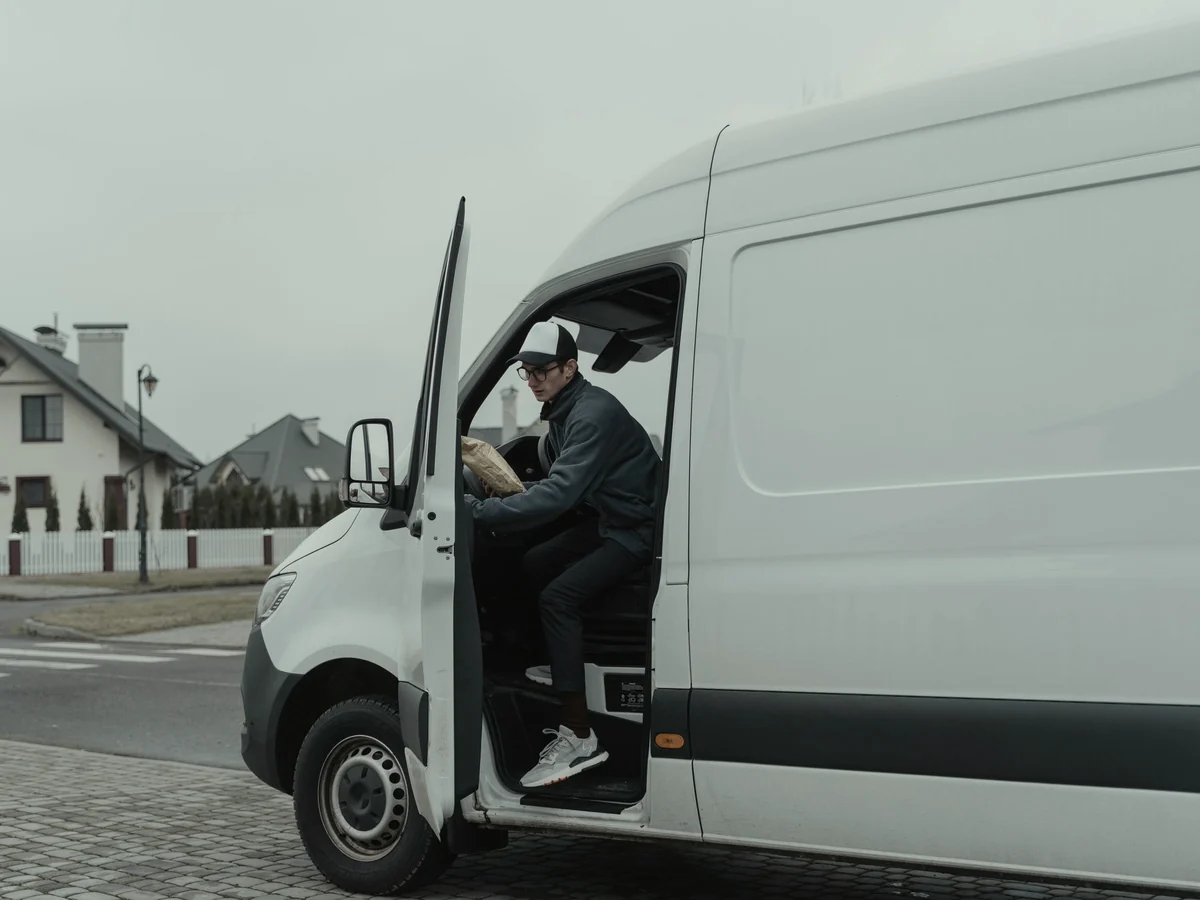 Driver stepping out of a white delivery van parked at a suburban kerb