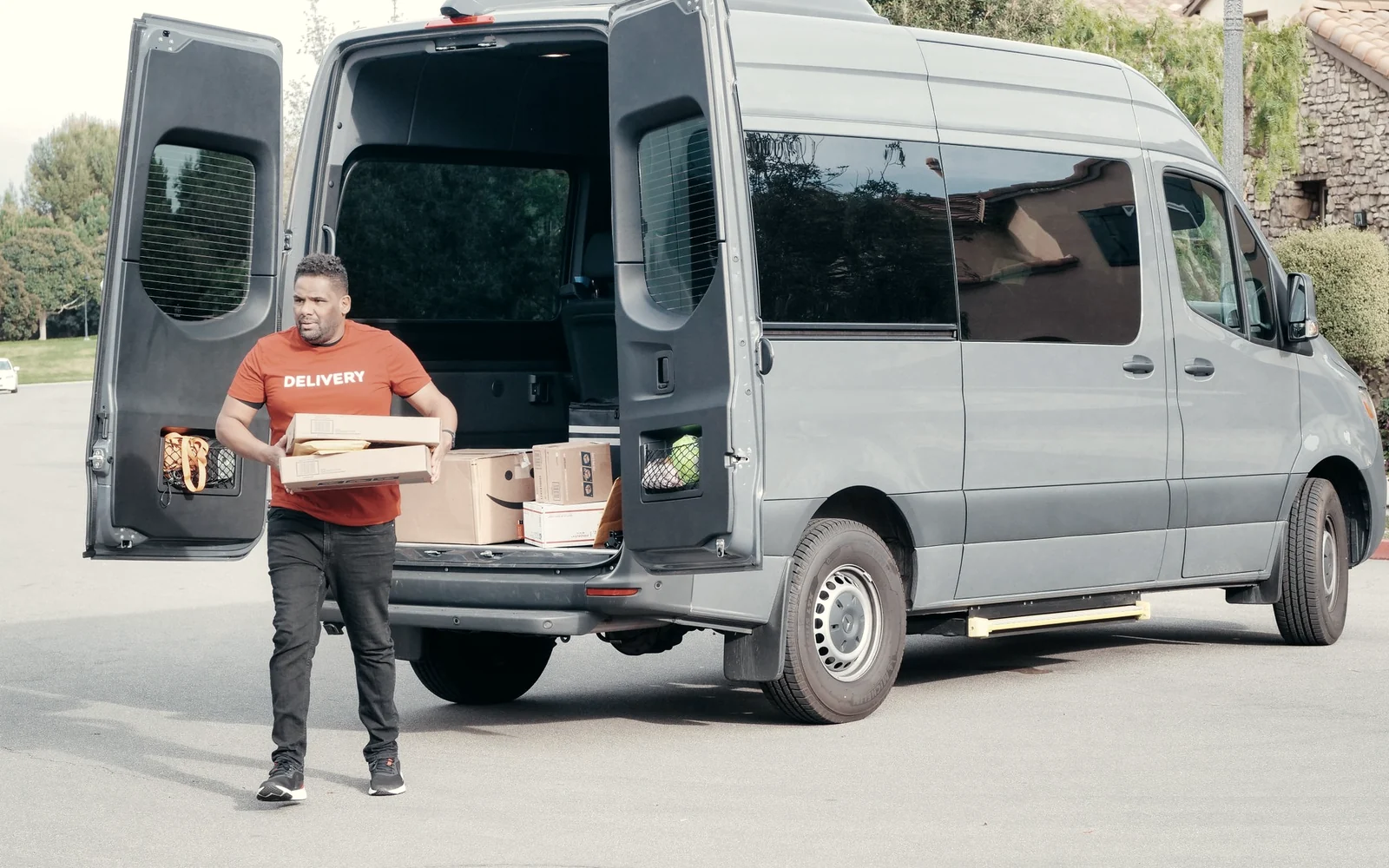 Courier carrying a parcel from the open rear doors of a grey transit van